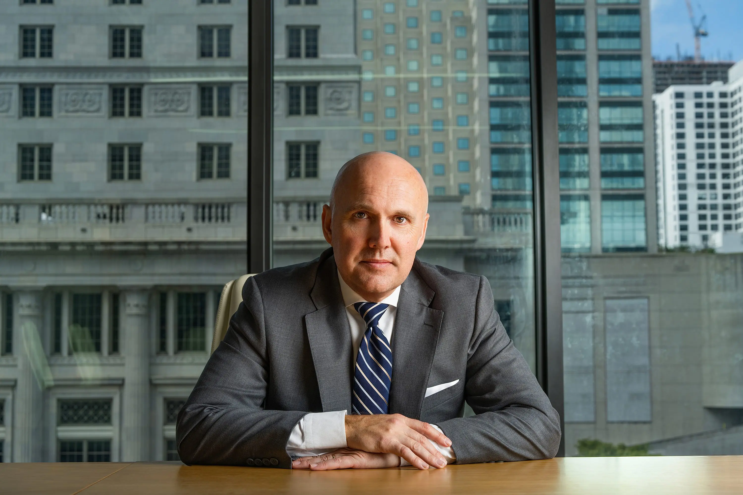 Businessman in suit sitting at a desk with city buildings in the background.
