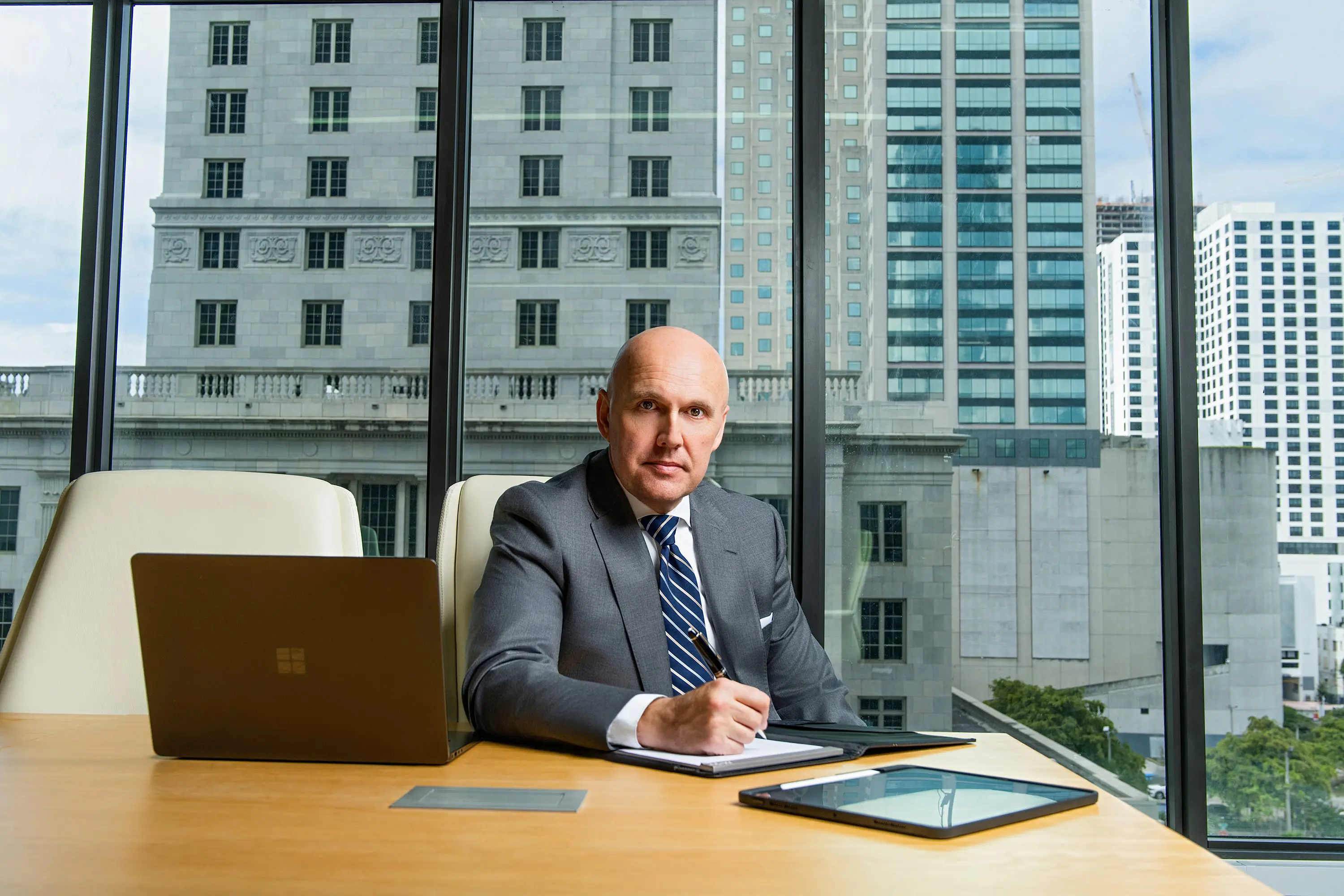 Businessman in a suit working at a desk with city buildings behind.