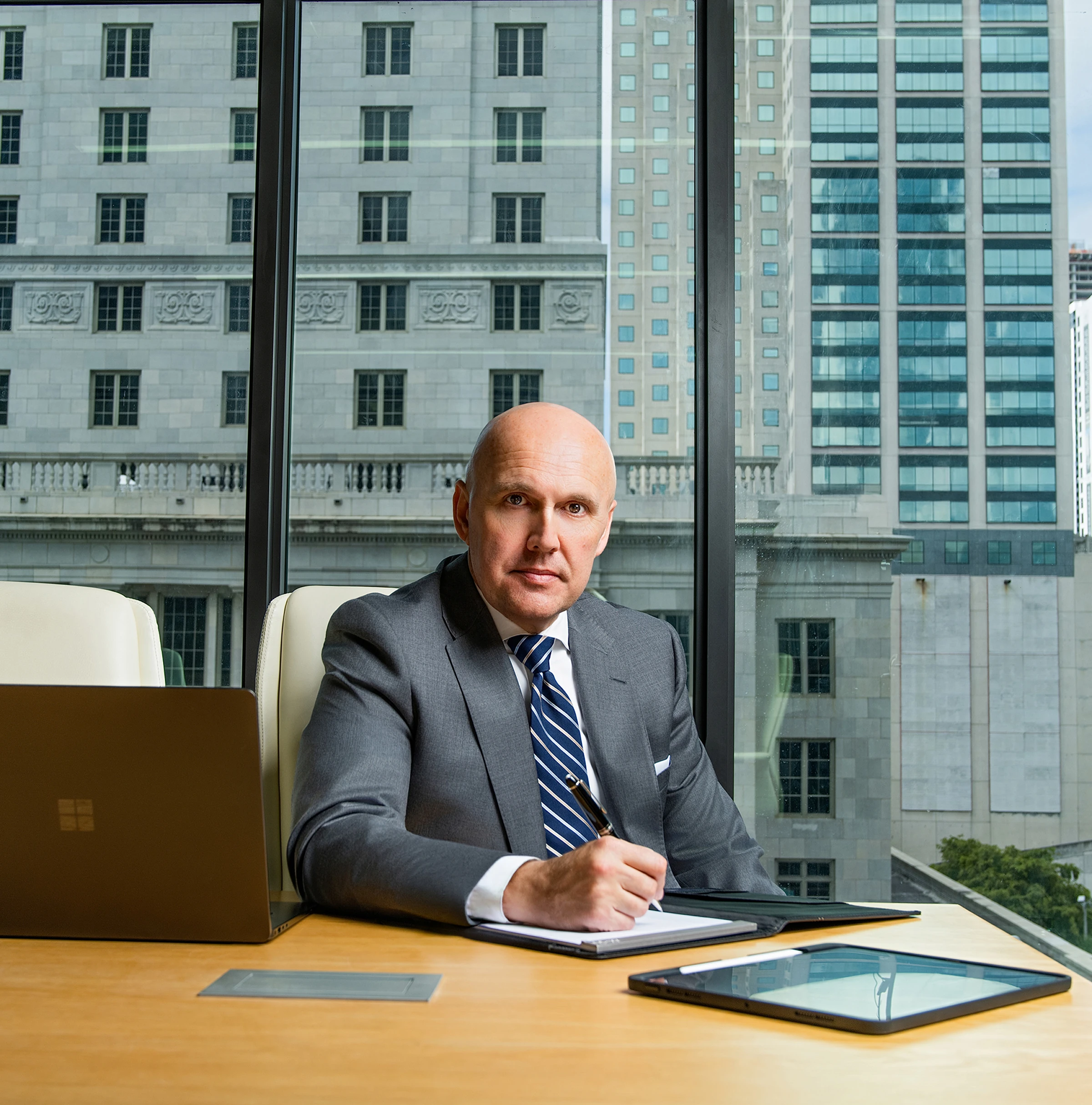 Confident businessman sitting at desk in office with city view.