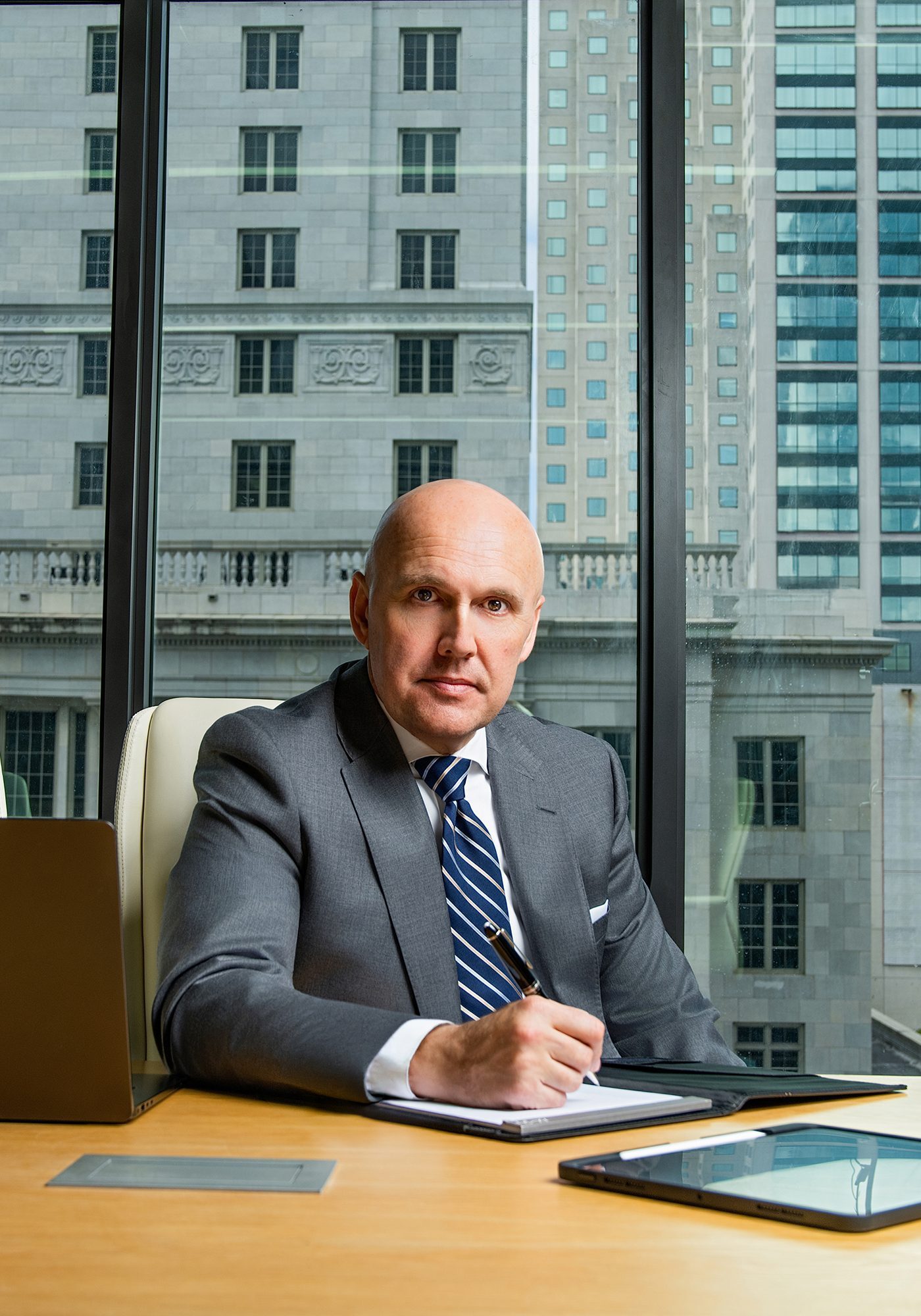 Businessman in a suit working at his desk with city buildings behind him.